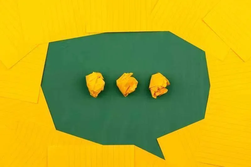 Balão de fala verde com três bolas de papel amassadas amarelas, cercado por papéis amarelos pautados
